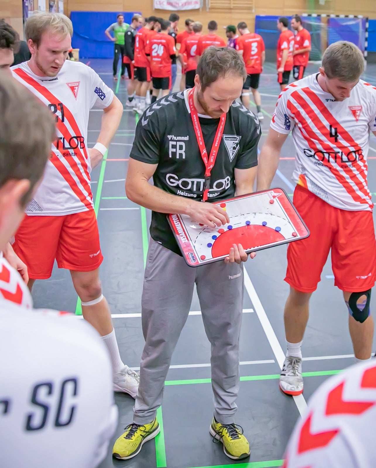 Handball-Taktikboard mit Tasten und Spielfeld in der Hand, Trainer zeigt per Hand.