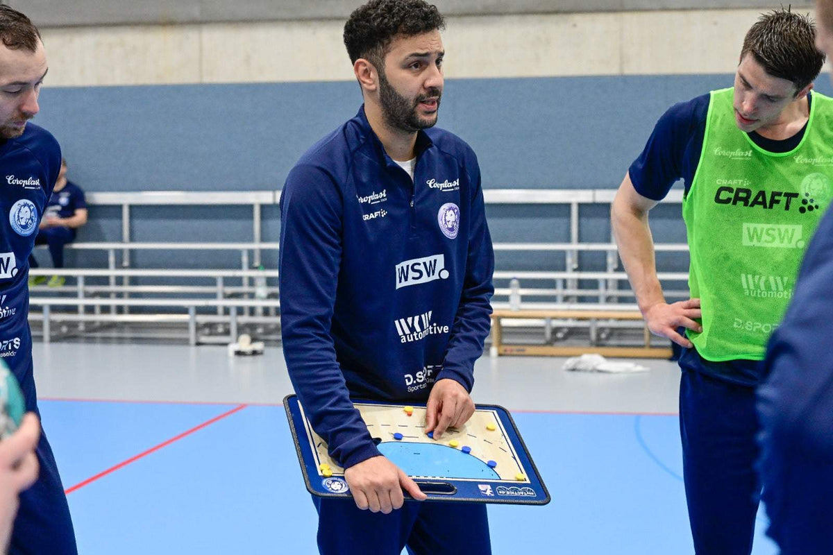 Handball-Taktikboard in Händen eines Trainers, Spielfeldmarkierungen auf blauem Untergrund.