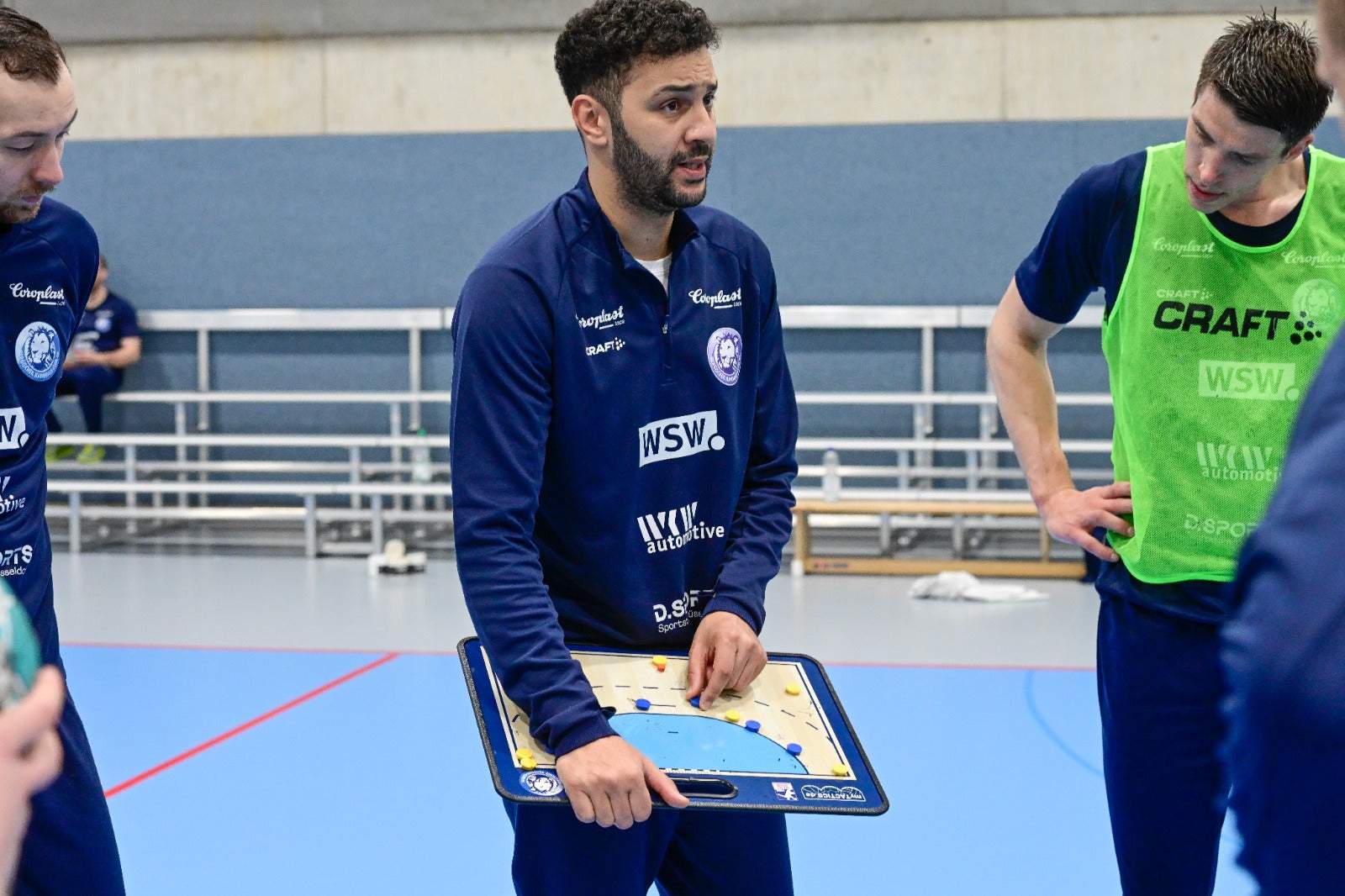 Handball-Taktikboard in Händen eines Trainers, Spielfeldmarkierungen auf blauem Untergrund.